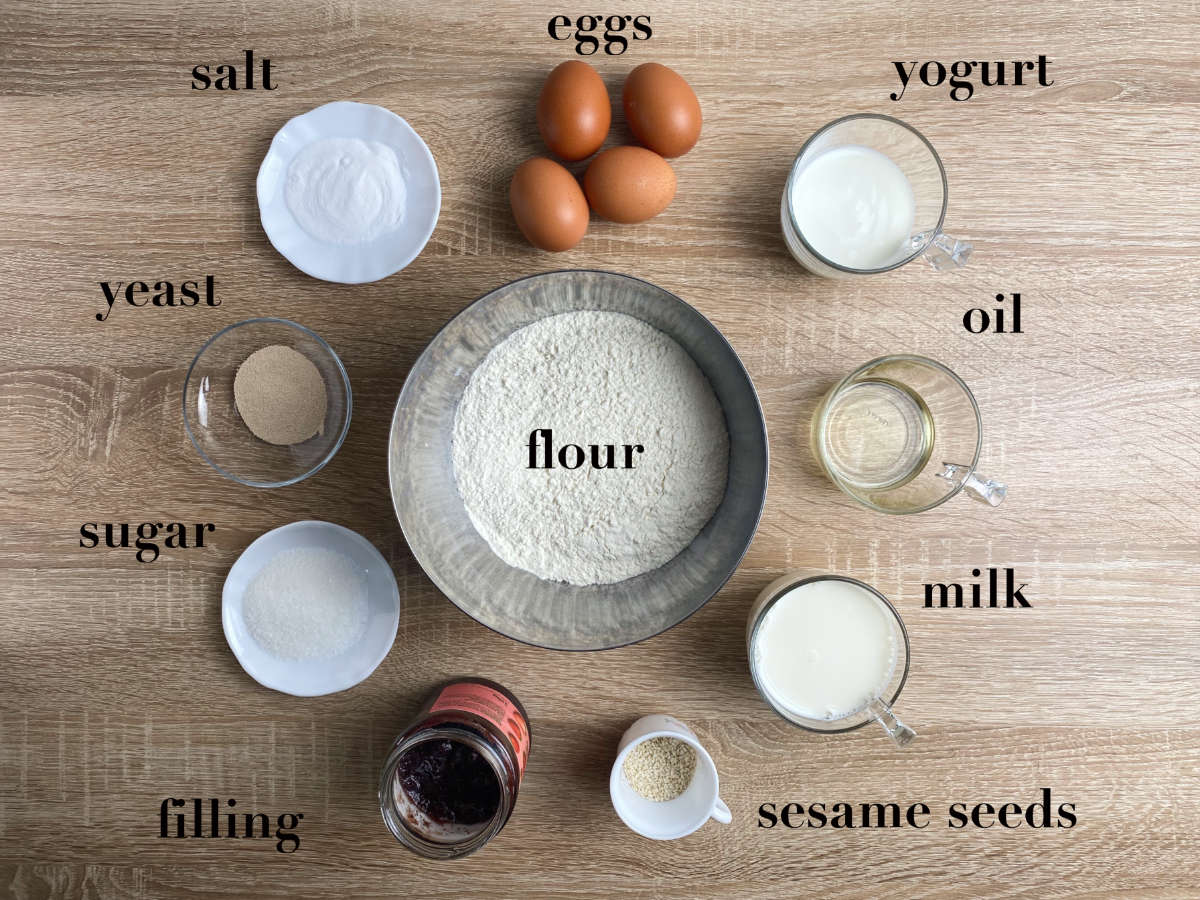 Overhead photo of ingredients for bread on a table: yeast, flour, salt, filling, yogurt, milk eggs, sugar and oil.