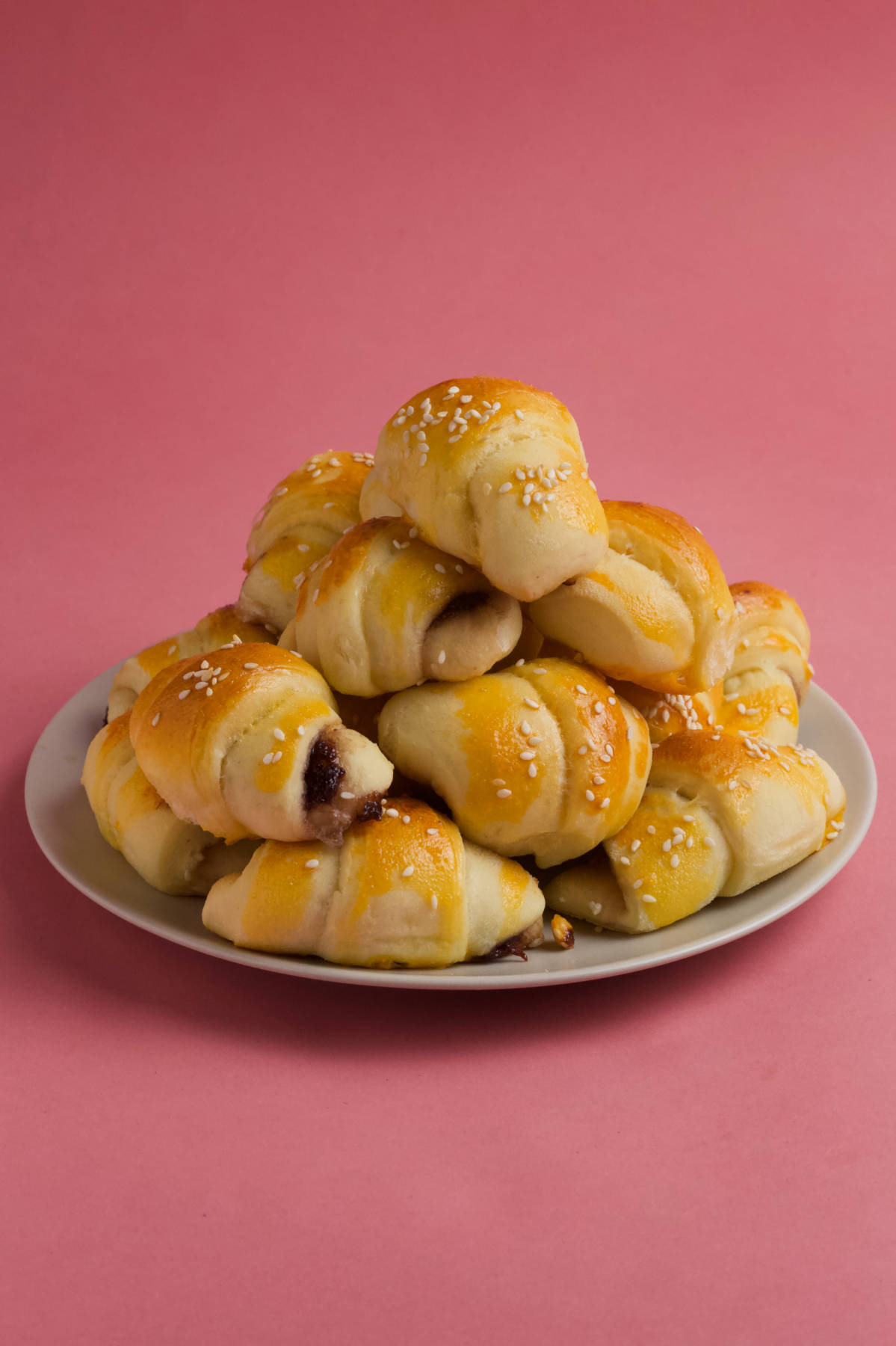 A plate holding crescent rolls on a pink background..
