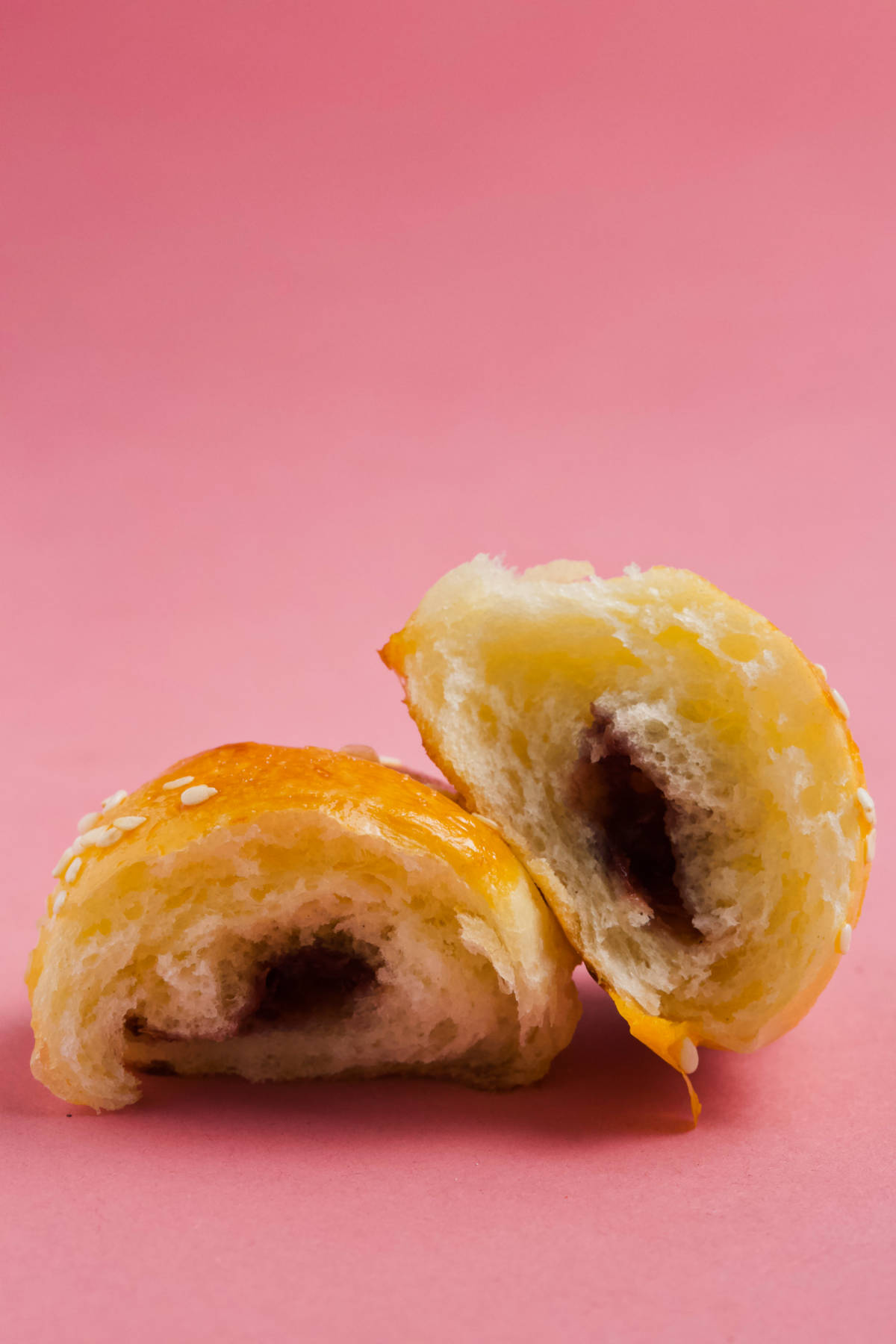A crescent roll, halved, on a pink background.