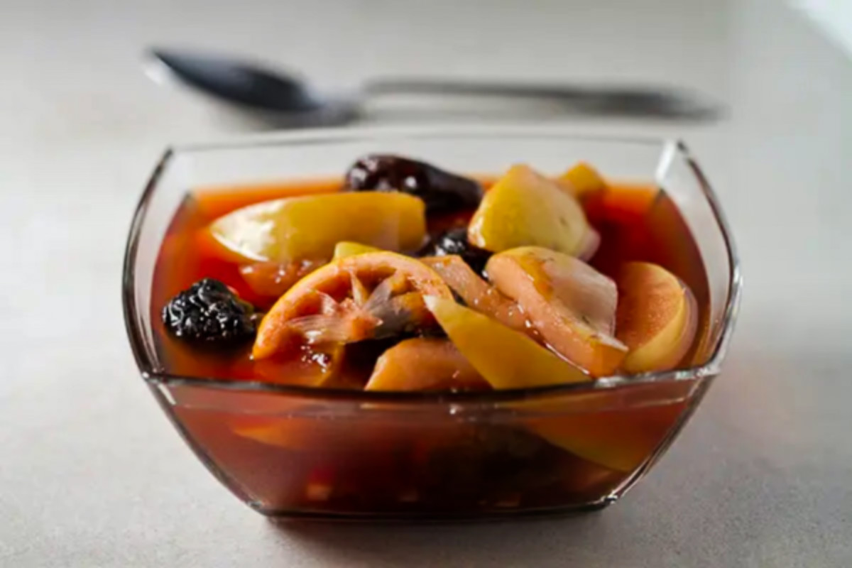 Compote in a glass bowl on a gray background, spoon in the background.