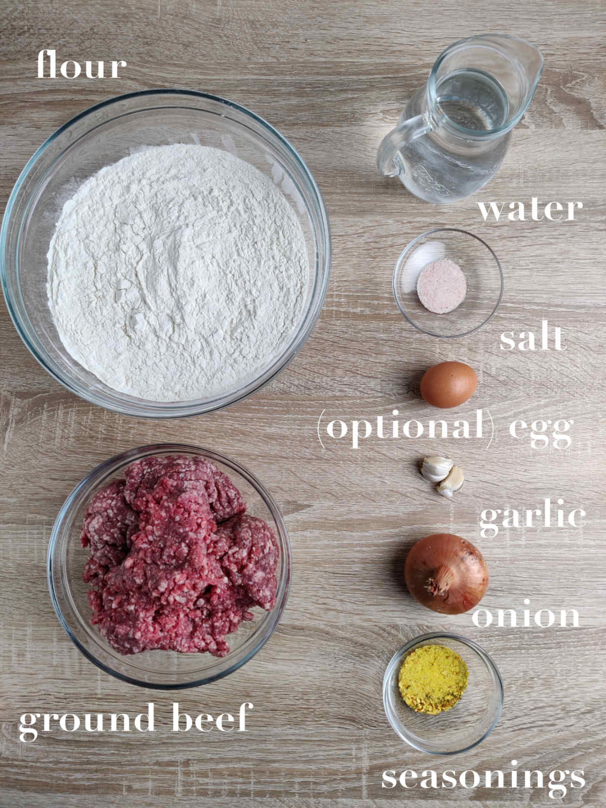 Ingredients on a table (flour, ground meat, salt, egg, garlic, onion, seasonings). 