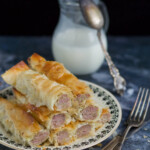 Rolls of pie on a plate, utensils, and pitcher with milk on dark background.