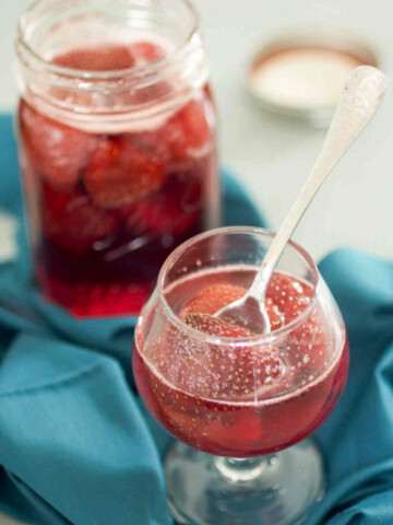 Jar and cup of strawberry syrup on a blue background.