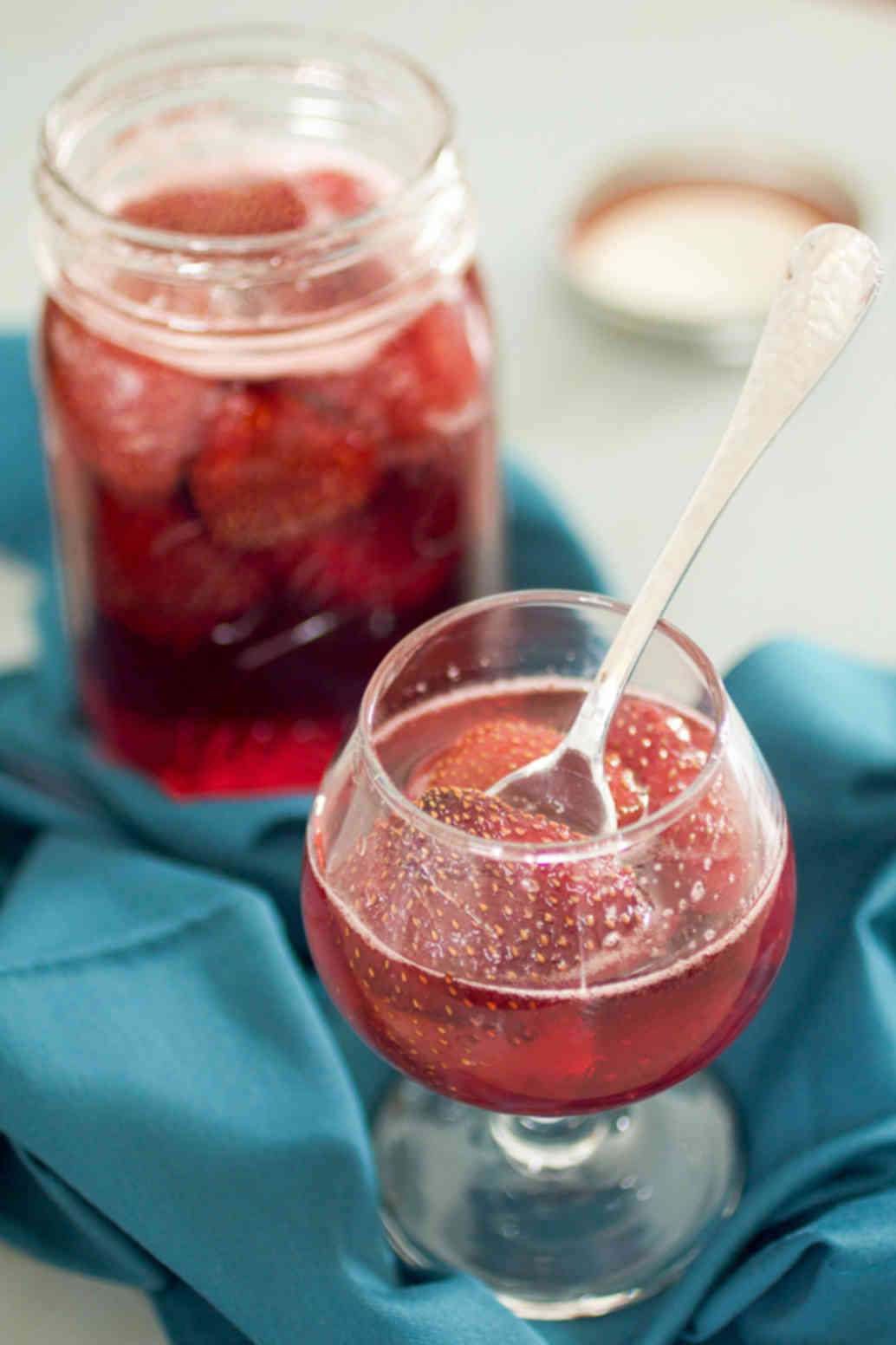 Jar and cup of strawberry syrup on a blue background.
