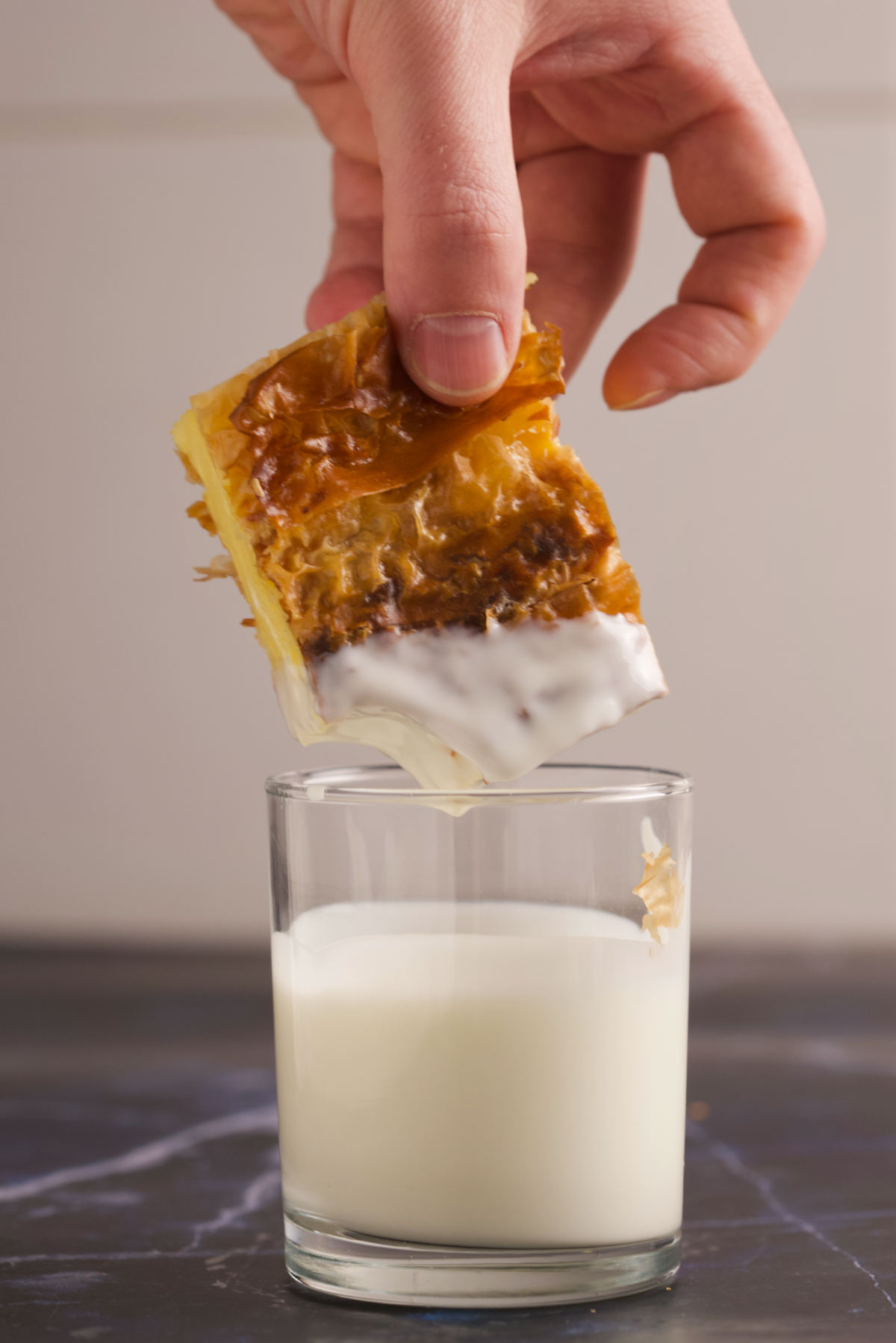 Hand holding a piece of pie above a glass of yogurt. 