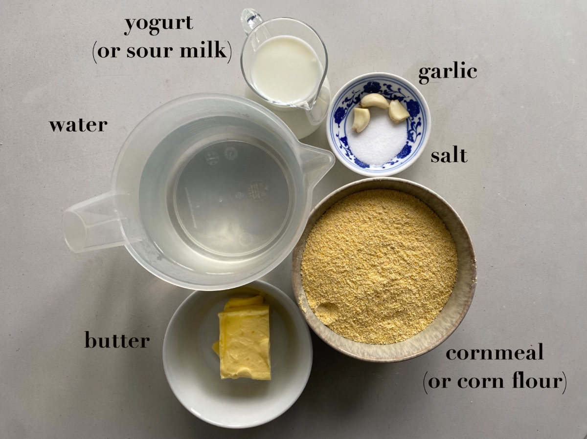 Ingredients in different types of containers on a gray background (yogurt, water, butter, corn flour, garlic, salt). 