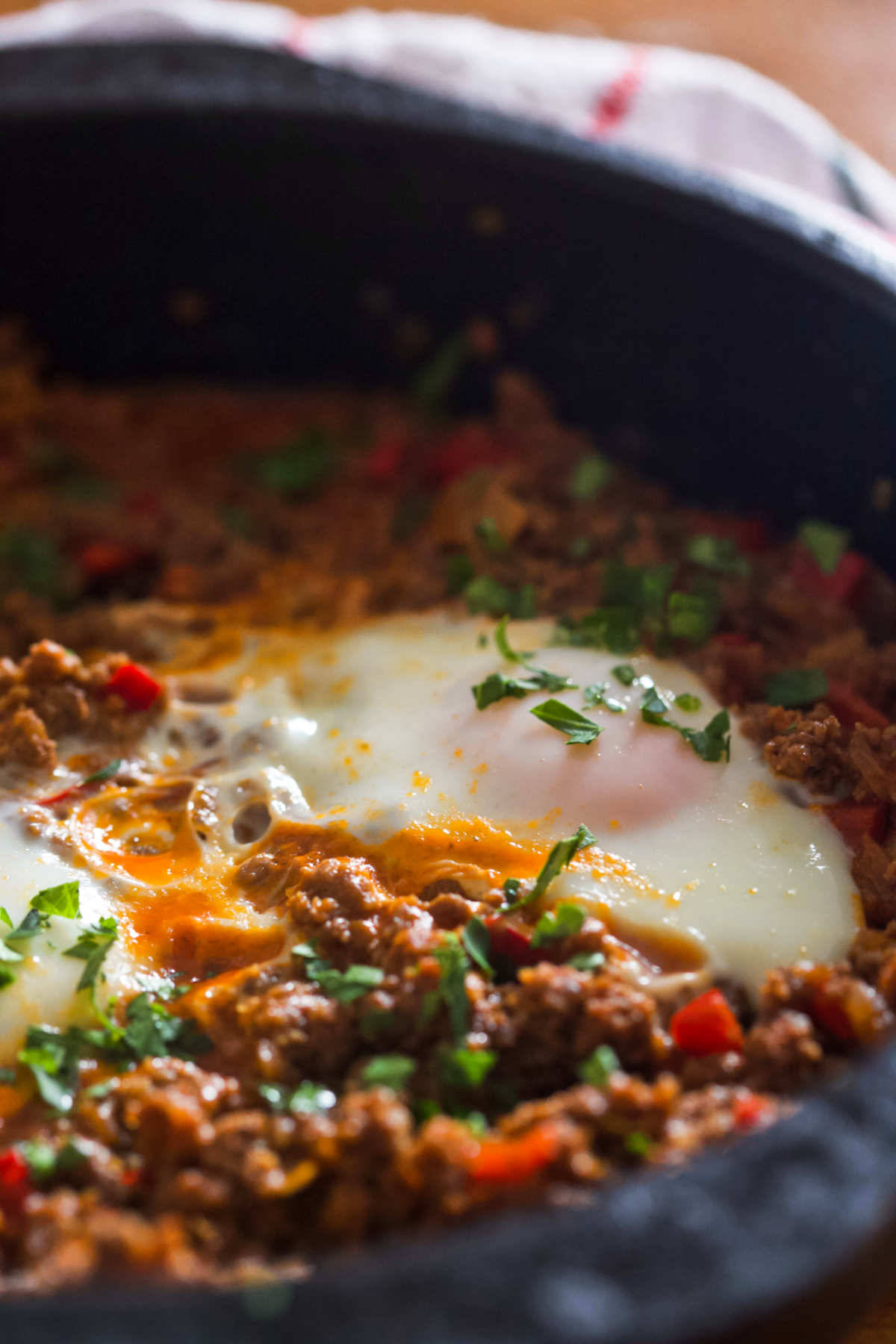 Closeup of two eggs on a bed of ground beef in a black pan on a wooden table. 