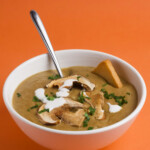 White bowl with a spoon and mushroom soup on an orange background.