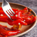 A fork holding red pepper salad above a plate on a marble table.