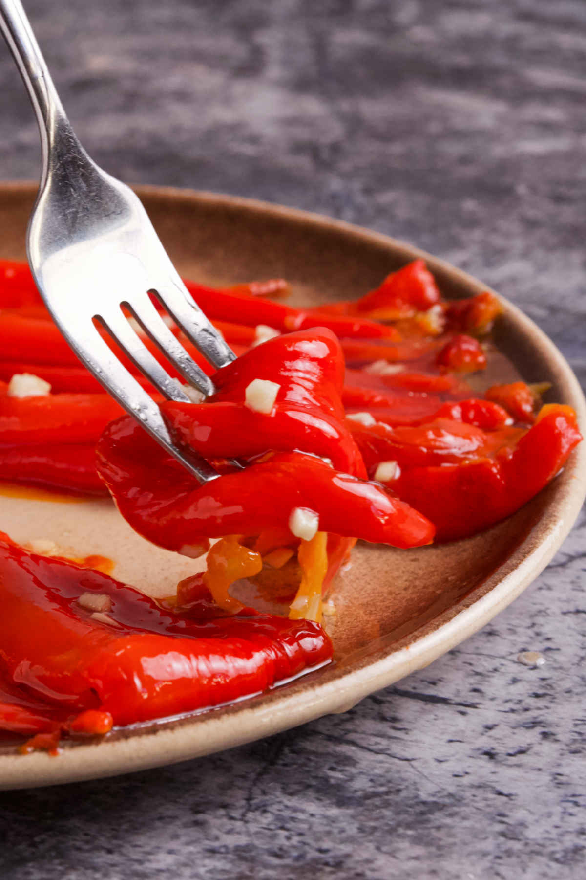 A fork holding red pepper salad above a plate on a marble table.