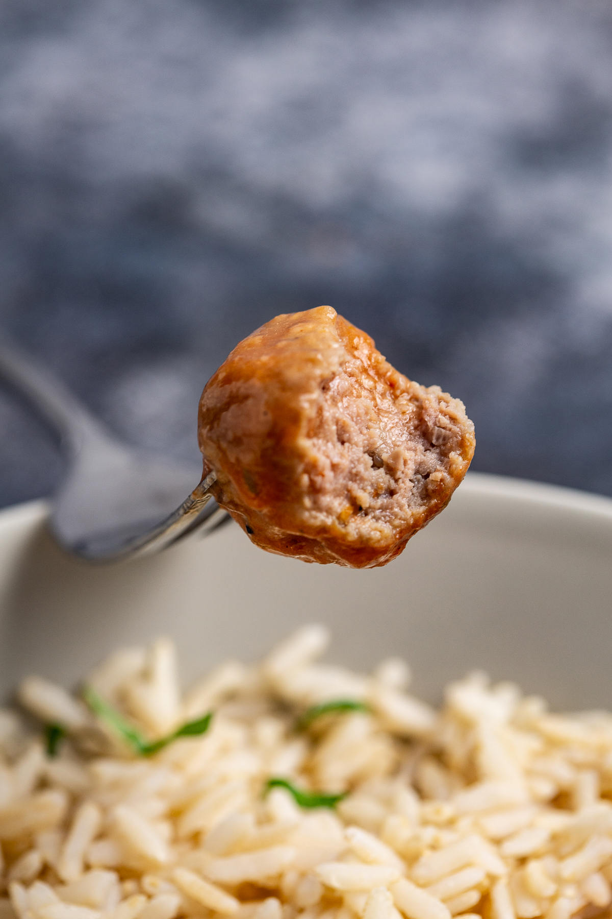 Meatball on a fork over a bowl of rice. 