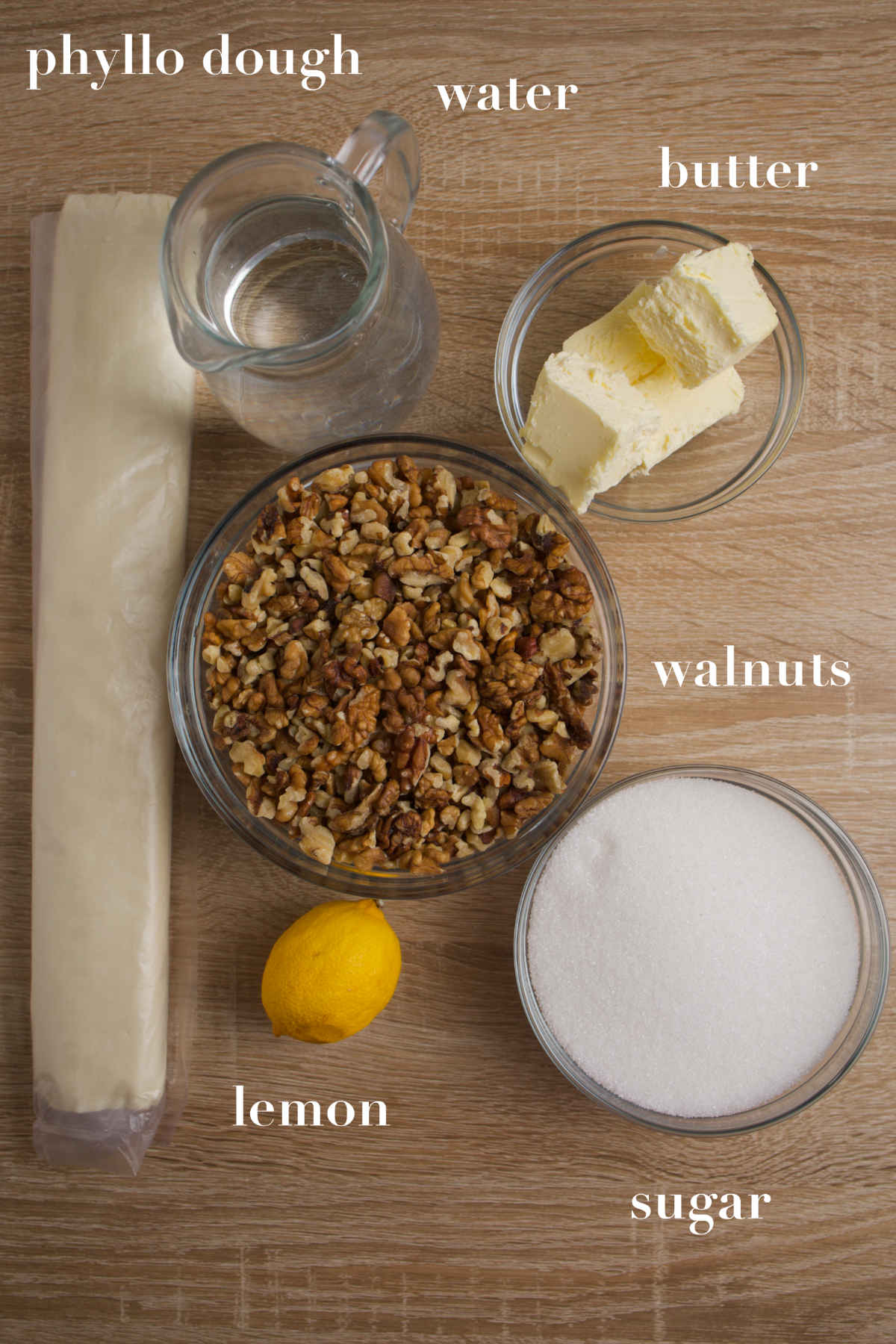 Phyllo dough, lemon, sugar, walnuts and butter on a wooden table.