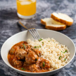 Plate with meatballs and rice, glass of juice and bread on a gray background.