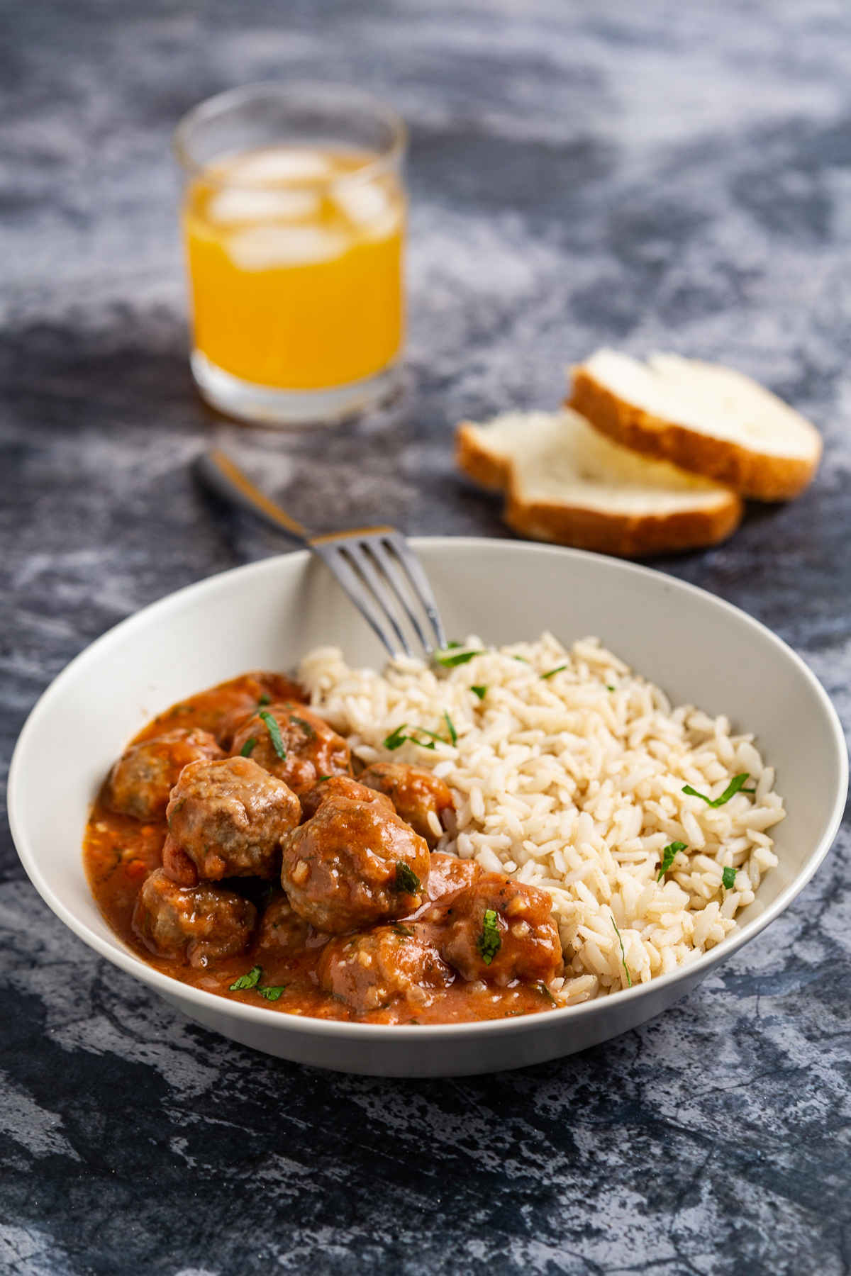 Plate with meatballs and rice, glass of juice and bread on a gray background.