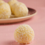 Coconut ball on a pink background with a coconut ball plate in the background.