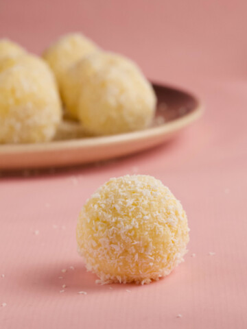 Coconut ball on a pink background with a coconut ball plate in the background.