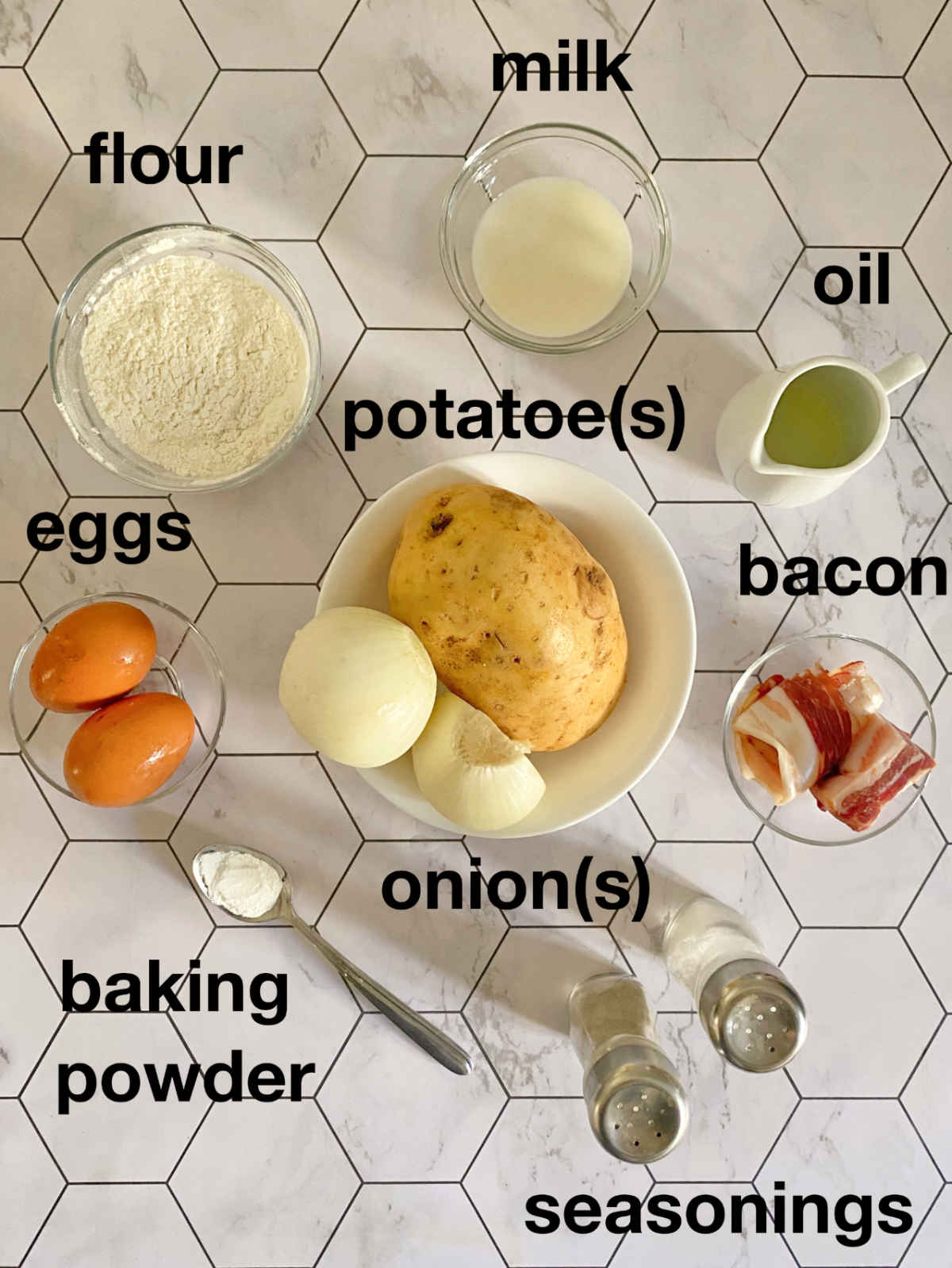 Overhead photo: flour, milk, potatoes, onions, bacon, seasonings and baking powder in different bowls on a honeycomb white background.