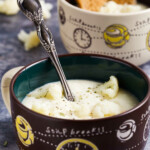 Two bowls (brown and beige) with creamy cauliflower soup on a gray marble background.