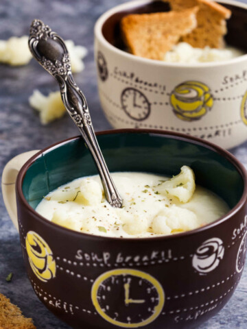 Two bowls (brown and beige) with creamy cauliflower soup on a gray marble background.