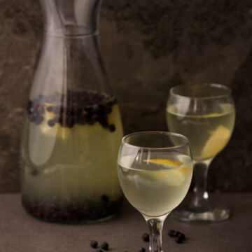 Two glasses and a glass bottle with juice on a dark background.