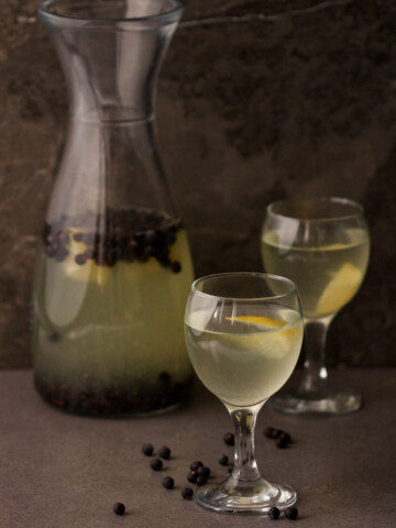 Two glasses and a glass bottle with juice on a dark background.