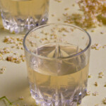 Two glasses of elderflower cordial on a lime background.