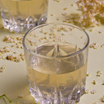 Two glasses of elderflower cordial on a lime background.