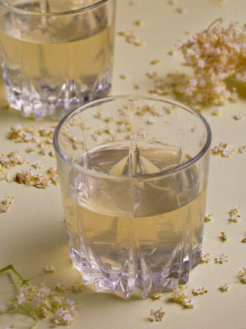 Two glasses of elderflower cordial on a lime background.