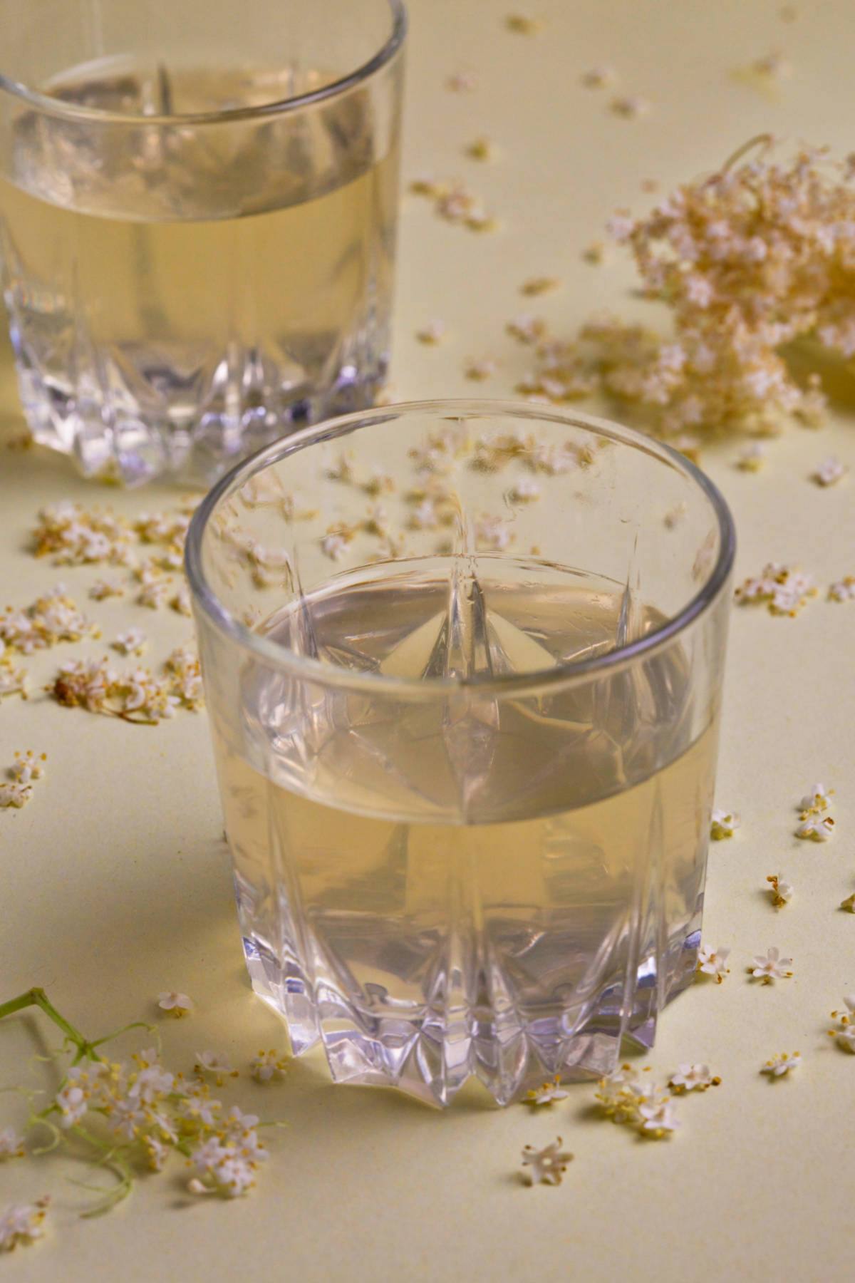 Two glasses of elderflower cordial on a lime background. 