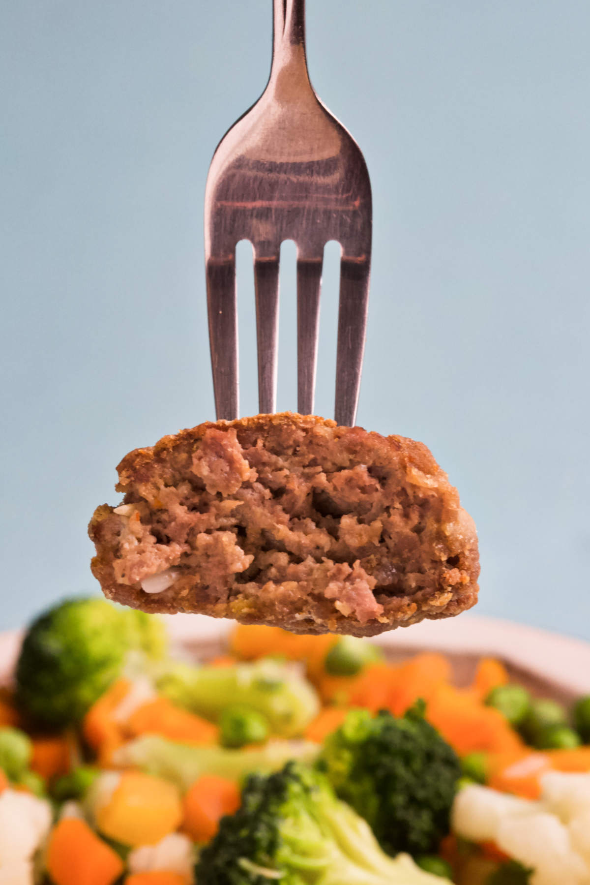 A fork holding a rissole above veggies.