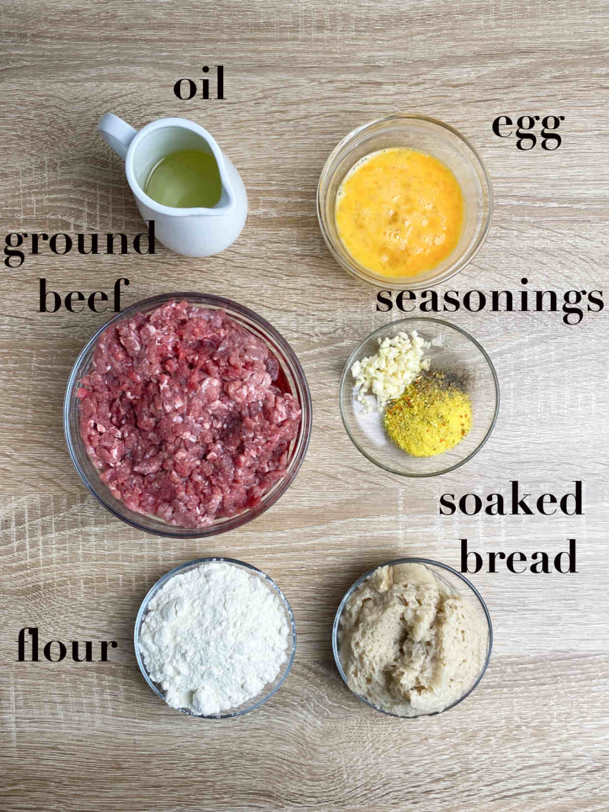 Six ingredients on top of the table (oil, egg, seasonings, ground beef, flour, soaked bread).