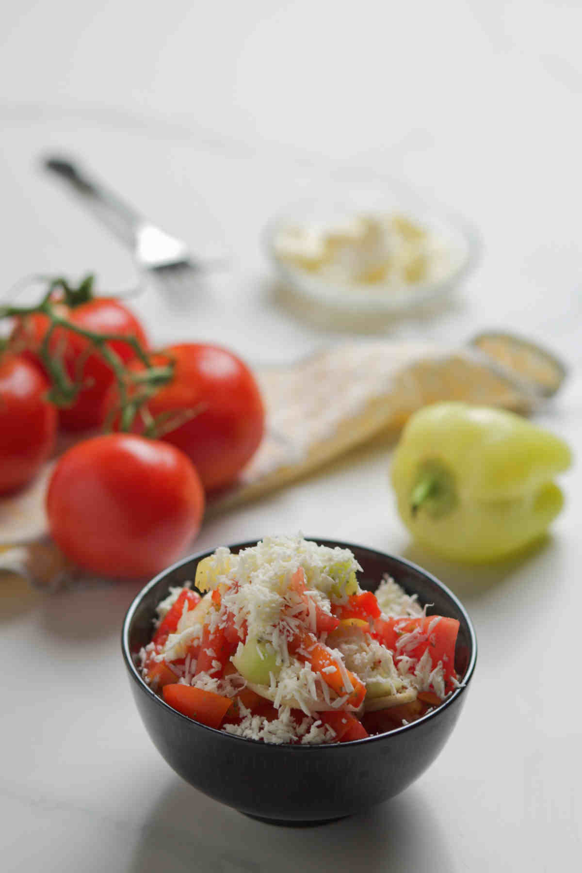 Bowl of salad, tomatoes on vine, fork, napkin, bell pepper and grated cheese  on white background. 