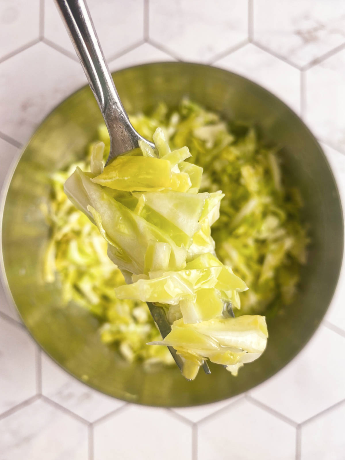 A stainless steel bowl with cabbage salad and a fork above it holding more salad.