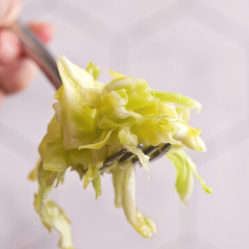 A hand holding a forkful of cabbage salad.