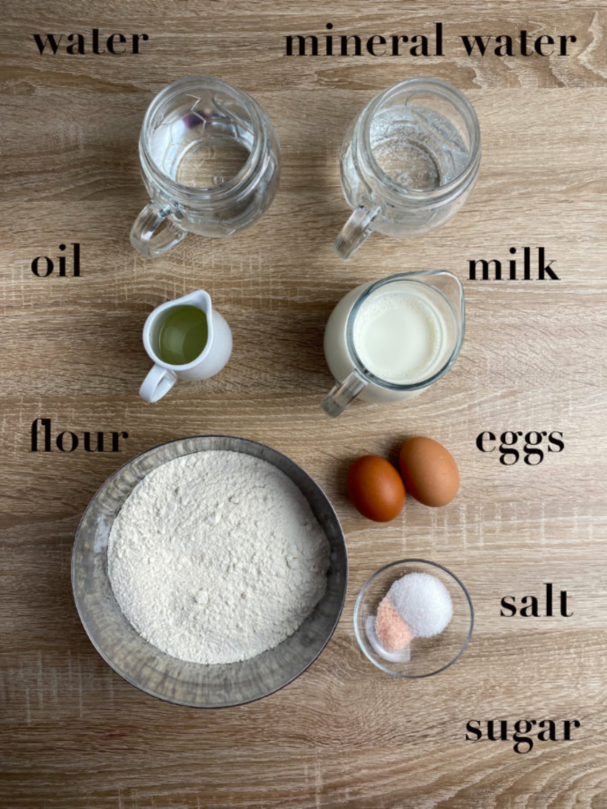 Ingredients on a wooden table - water, milk, mineral water, oil, eggs, salt, sugar and flour.