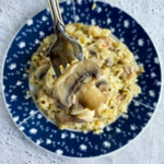 Overhead photo of a bowl of risotto and a fork holding risotto above it on a marble background.