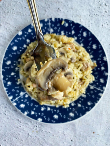 Overhead photo of a bowl of risotto and a fork holding risotto above it on a marble background.