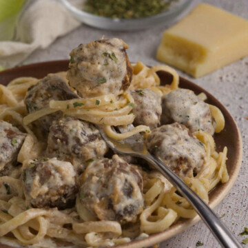 Plate full of meatballs and linguini, and a fork with a meatball.