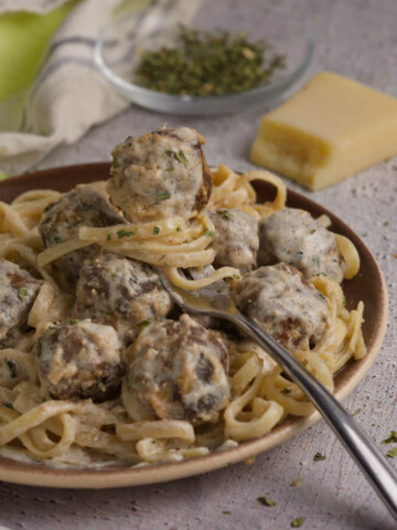 Plate full of meatballs and linguini, and a fork with a meatball.