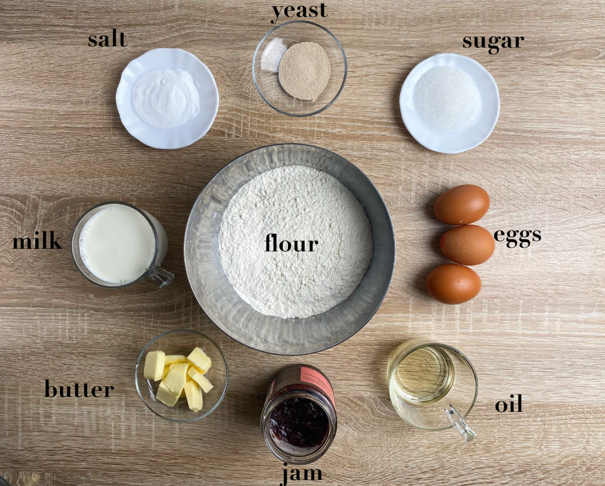 Overhead ingredients for jam rolls: salt, yeast, sugar, eggs, four, butter, jam, oil and milk. 