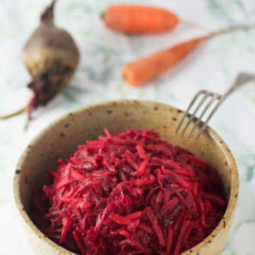 A bowl of carrot and beet salad, a beet, carrots and fork on the side.