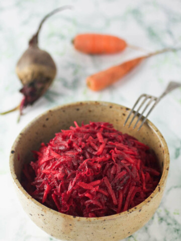 A bowl of carrot and beet salad, a beet, carrots and fork on the side.