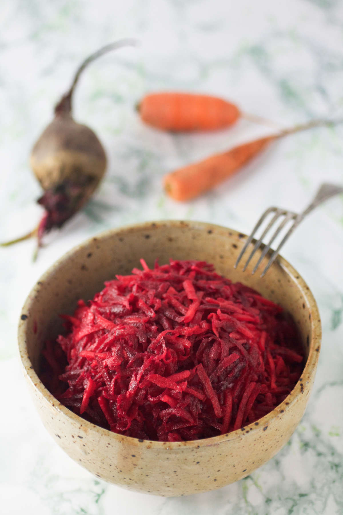 A bowl of carrot and beet salad, a beet, carrots and fork on the side. 