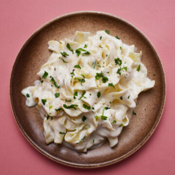 Milk pasta on a plate on a pink background, overhead photo.