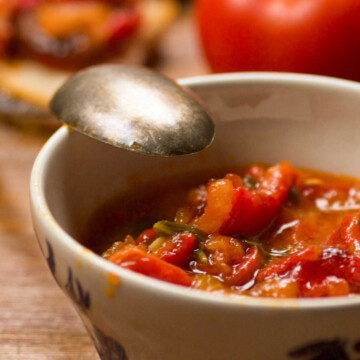 PIndjur in a bowl on a table with vegetables in the background.