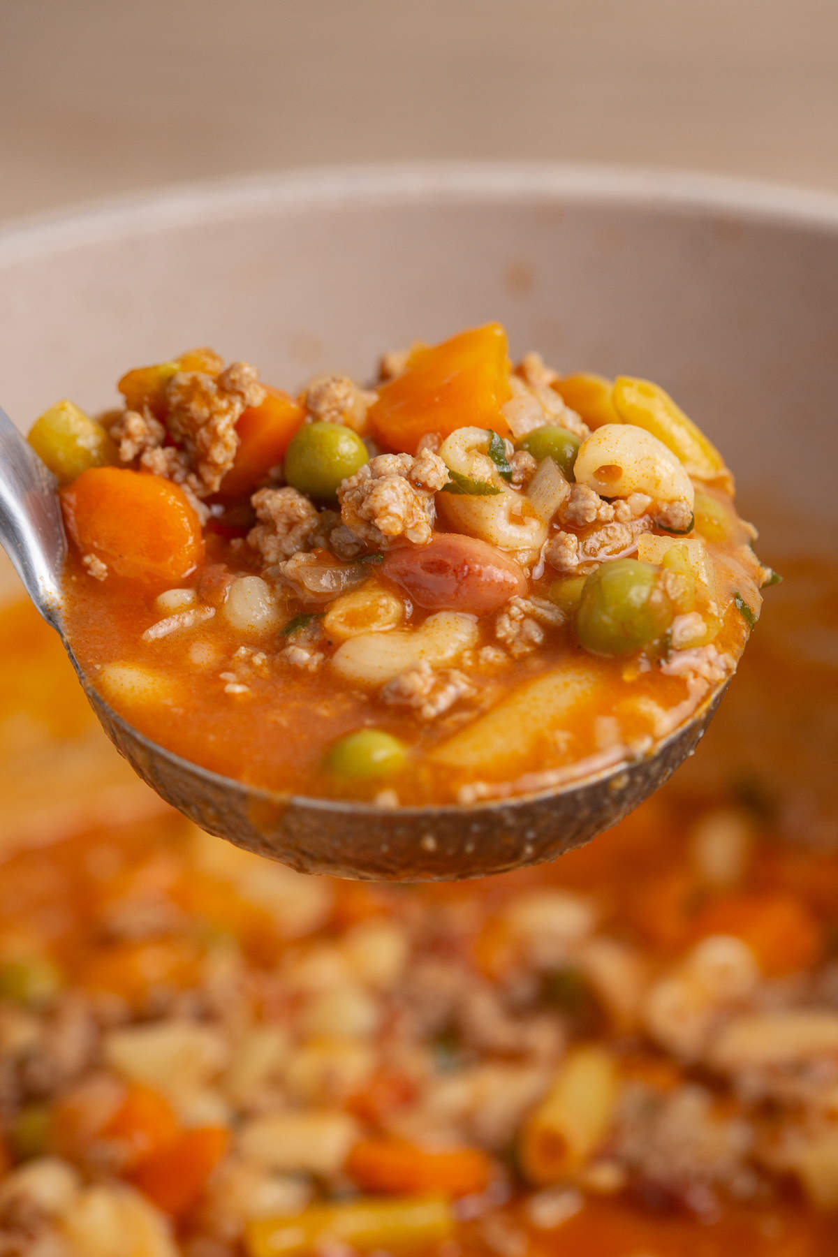 Ladle full of soup above a pot full of soup.