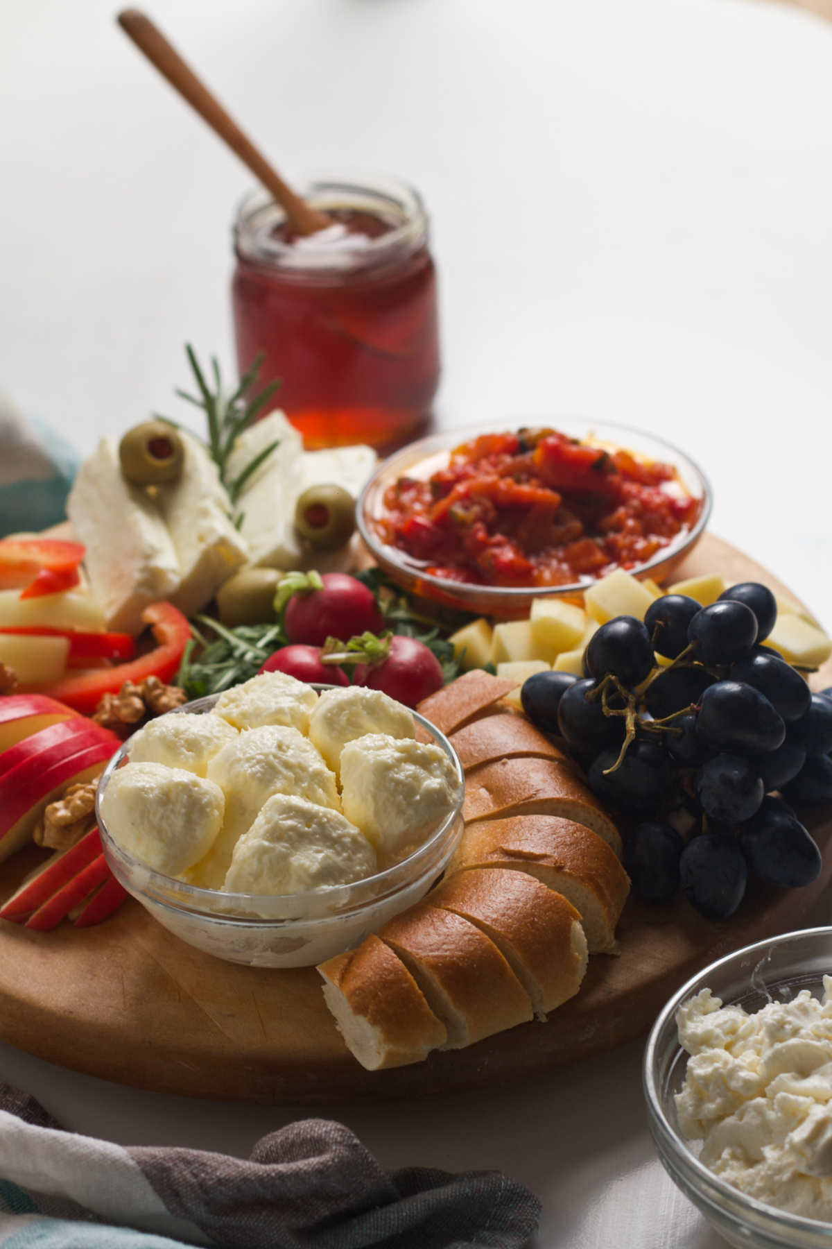 Wooden, round tray filled with different ingredients like ajvar, cheese, bread, grapes, meat, with a jar of honey in the distance.