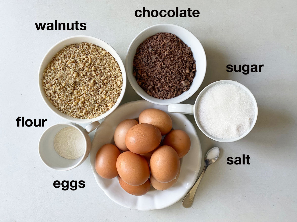 Ingredients for cake biscuit on a white background: walnuts, chocolate, eggs, flour, salt and sugar. .