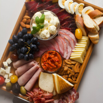 Overhead photo of a meat and cheese wooden tray platter on a gray background.