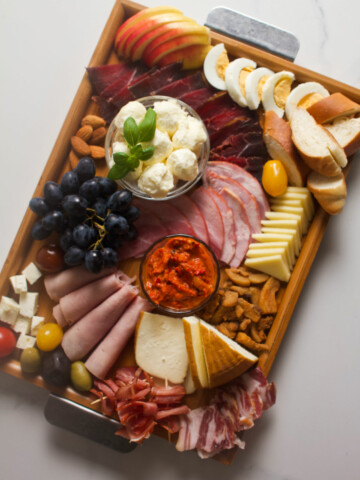 Overhead photo of a meat and cheese wooden tray platter on a gray background.